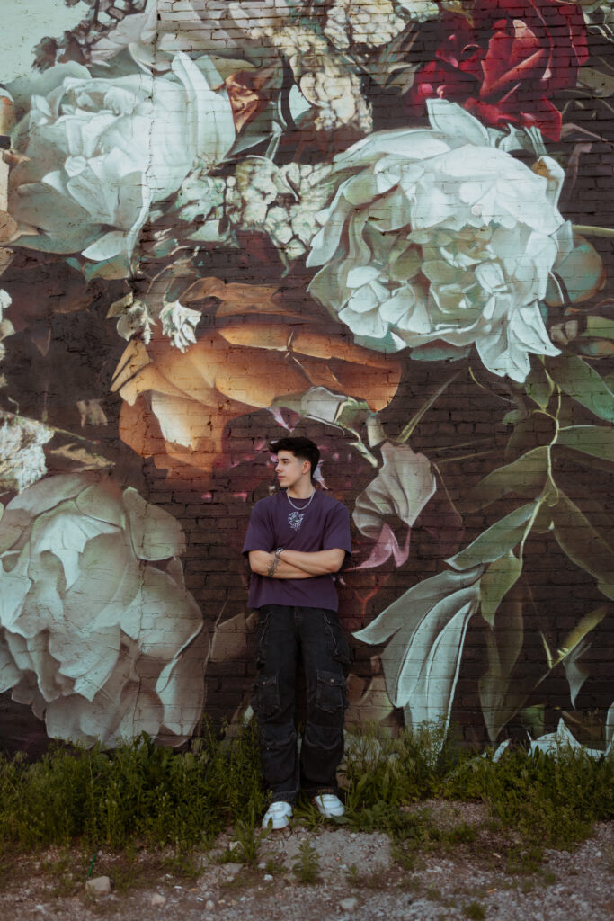 Senior guy in purple shirt poses and looks off to the side for a profile shot while leaning against a graffiti floral wall with senior portraits kansas city photographer.