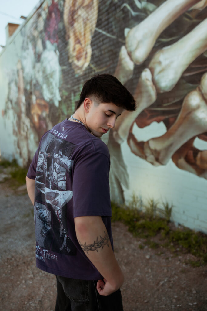 Senior guy in purple shirt looks over shoulder and down at the ground near a graffiti kansas city wall with senior portraits kansas city phogarapher.