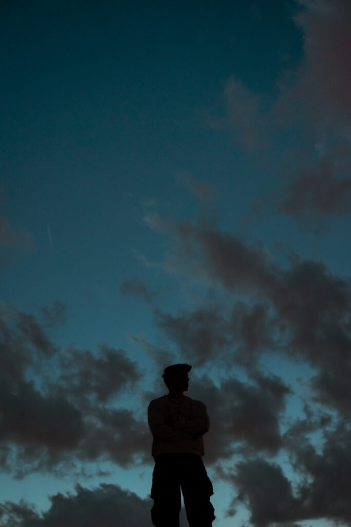 Silhouette shot of a senior guys profile against a dark blue cloudy sky for senior portraits in Kansas City.