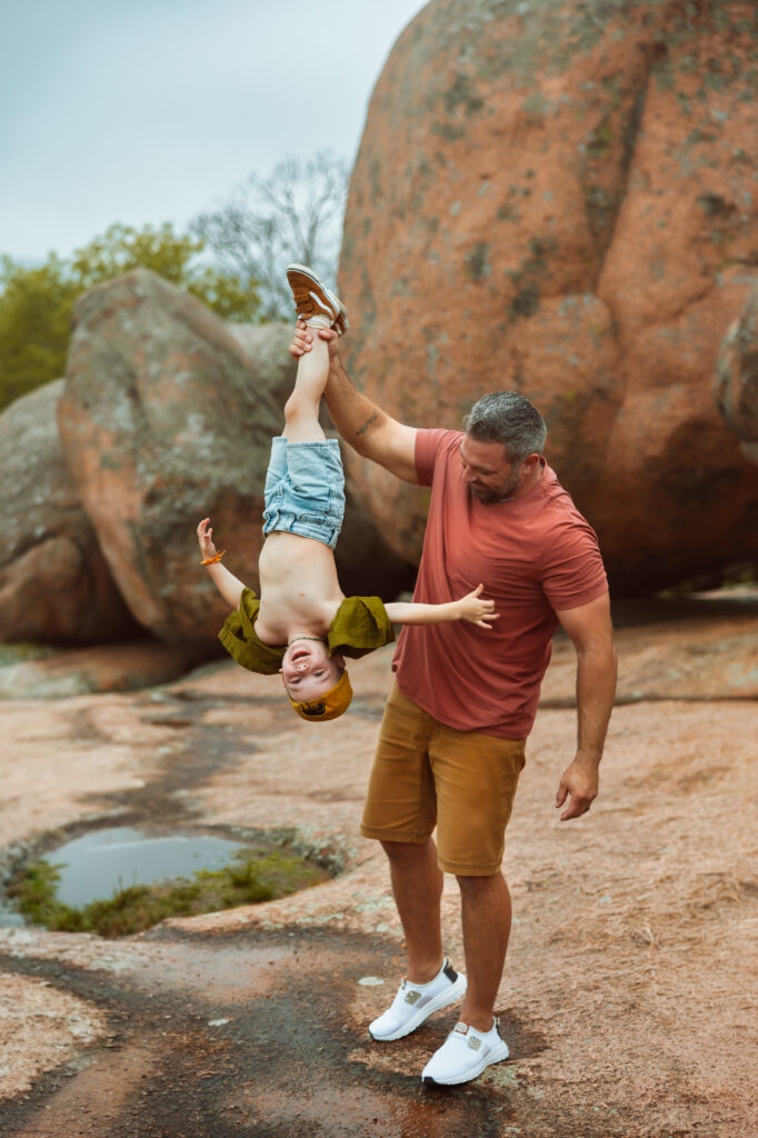 Dad holds his son upside down by his foot as his son giggles during family photos with Elephant Rocks State Park Family Photographers.