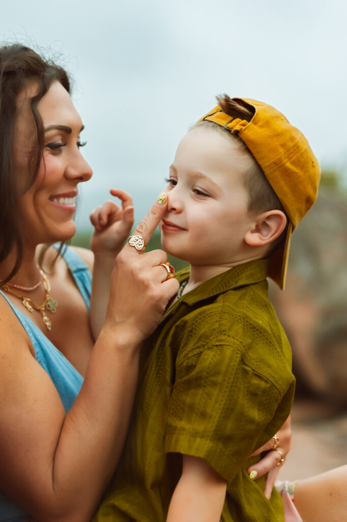 Mom in blue denim top taps her sons nose while he smiles big in a backwards yellow ball cap during family photos with Elephant Rocks State Park Family Photographers.
