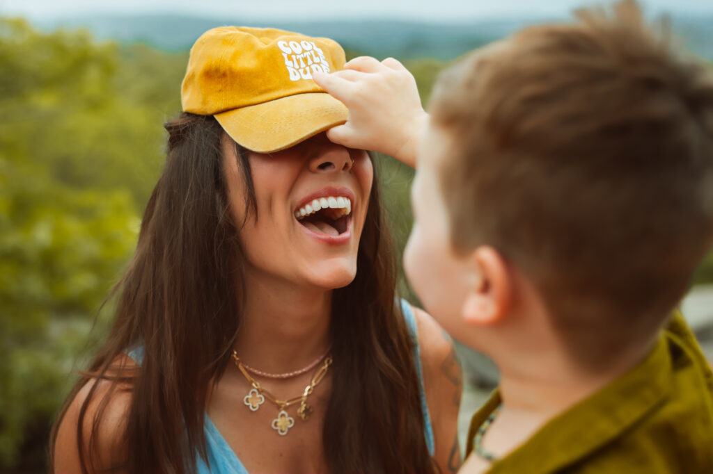 Mom laughs as son puts his bright yellow hat on his mom during a family photos with Elephant Rocks State Park Family Photographers.