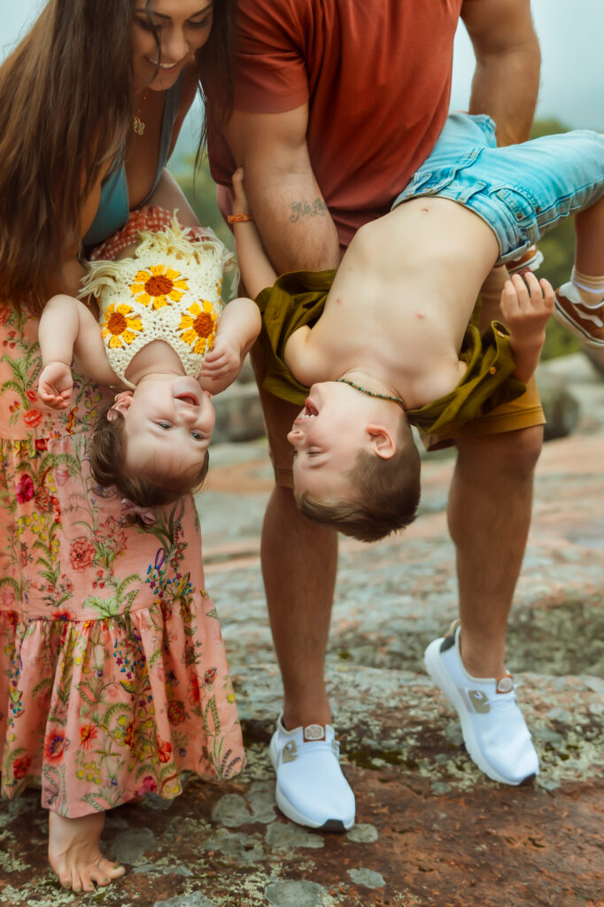Mom and dad dip their two children upside down while they look and giggle at each other during family photos with Elephant Rocks State Park Family Photographers.