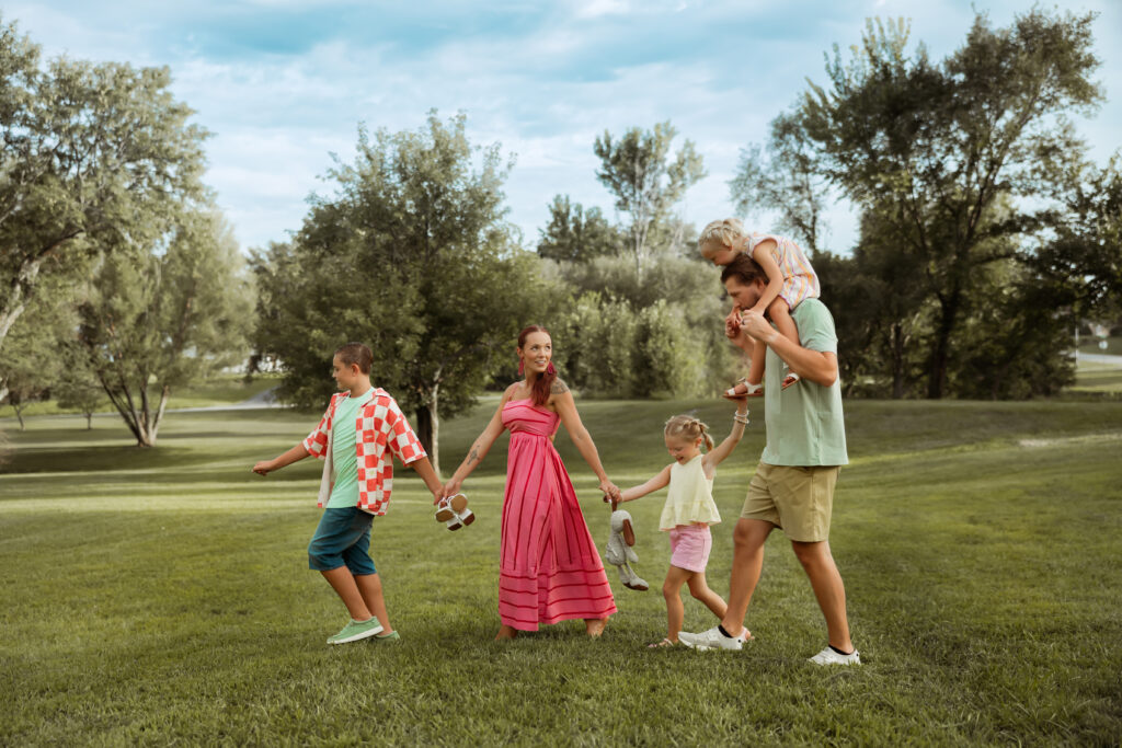 When searching Family Photos Near Me in Kansas City I hope you'll find this photo of a family of give walking through their back yard holding hands wearing bright pinks and summer greens.