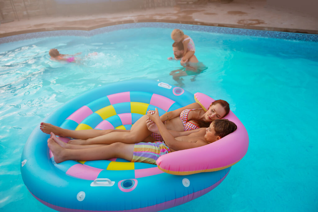 Searching Family Photos Near Me you'll find Kansas City Photographers that capture mom and her son talking in a colorful pool float while dad plays with the kids near by in their own back yard swimming pool during family photos.
